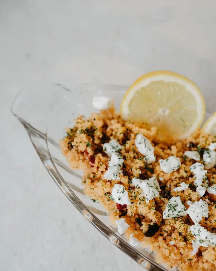 A homemade couscous dish topped with cheese and fresh lemon slices, perfect for a hearty meal.