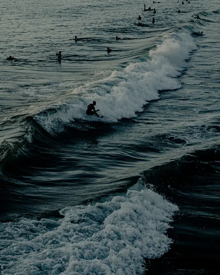 Silhouetted surfers ride waves at sunset, creating a dynamic ocean scene.
