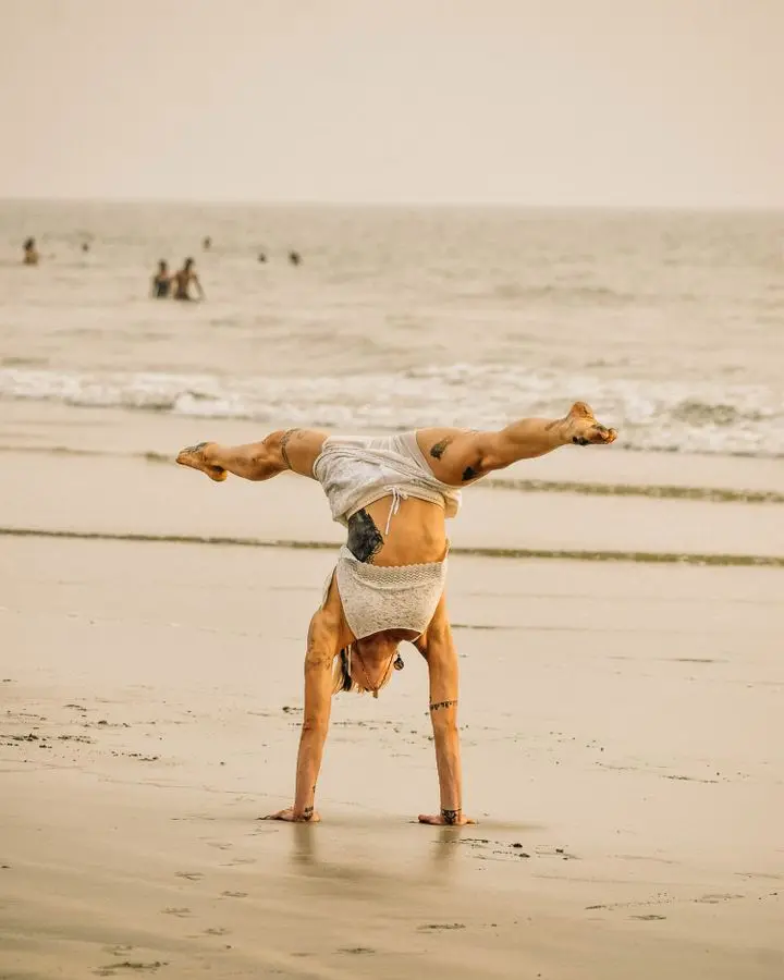 Man performs yoga handstand on a serene beach in Goa at sunset.