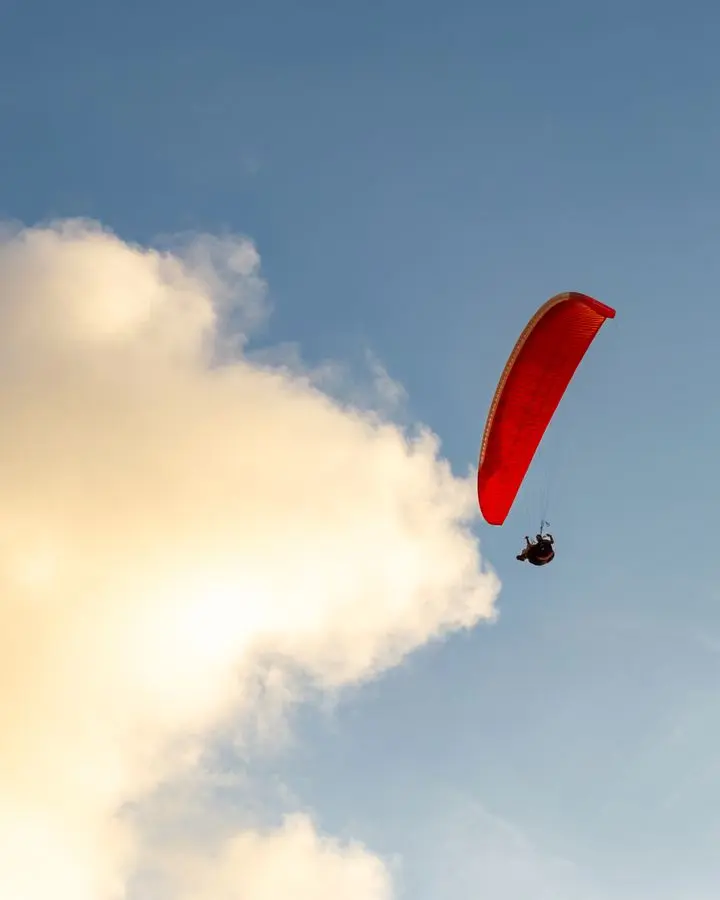 A lone paraglider with a red parachute glides gracefully against a picturesque sky in Brazil.