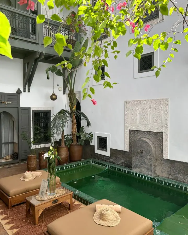 Charming Moroccan courtyard featuring a green pool, lush plants, and traditional architectural accents.