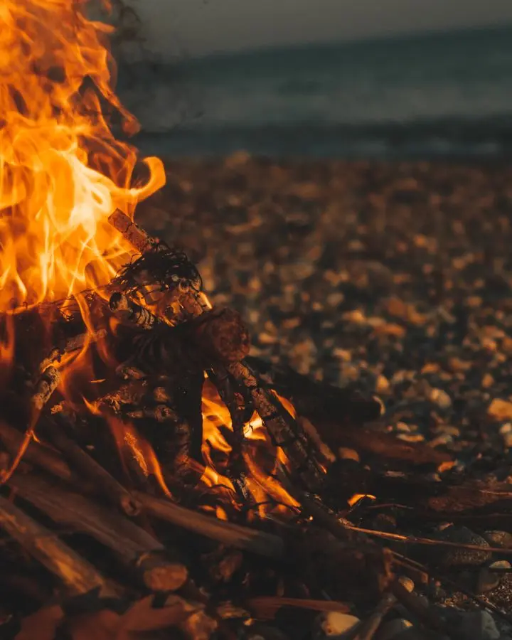 Warm bonfire flames lighting up a pebbly beach, creating a cozy outdoor evening ambiance.