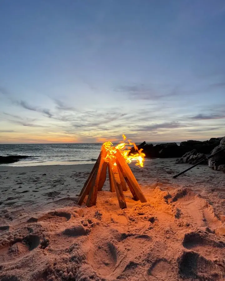 Tranquil beach bonfire with a stunning sunset over the ocean horizon.