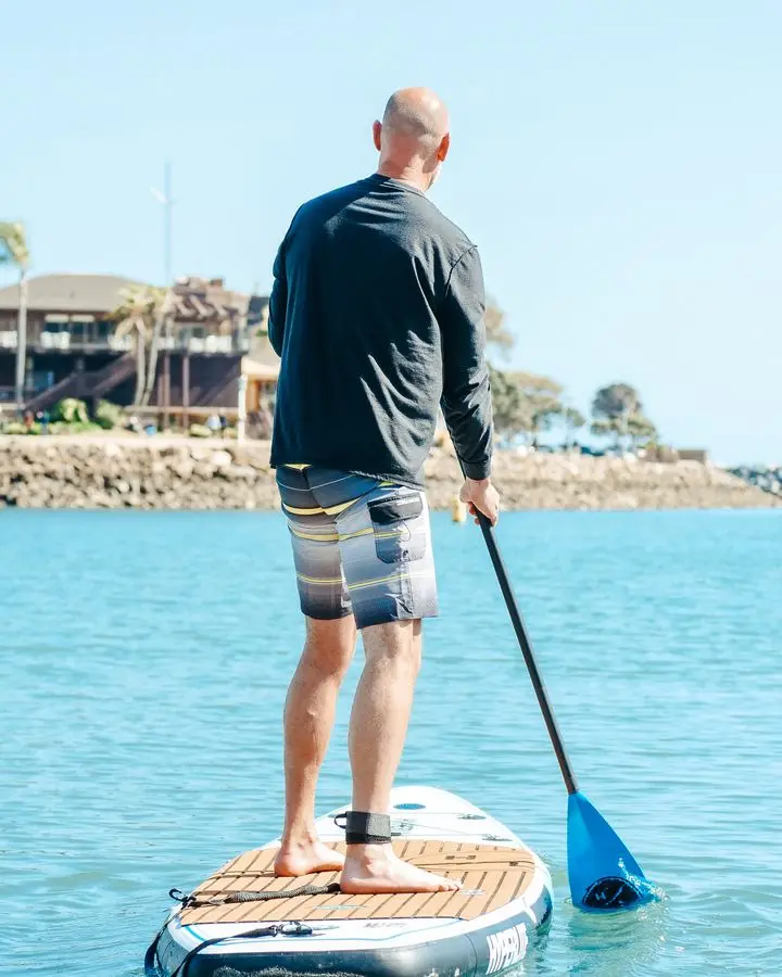 Man enjoying stand-up paddleboarding on a bright day by the ocean.